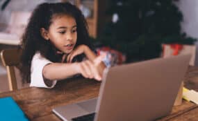 African American child sitting at wooden table with a laptop during an online therapy session