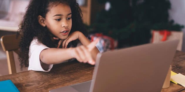 African American child sitting at wooden table with a laptop during an online therapy session