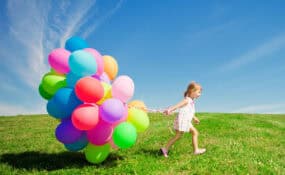hapopy little girl holding colorful balloons on a green field