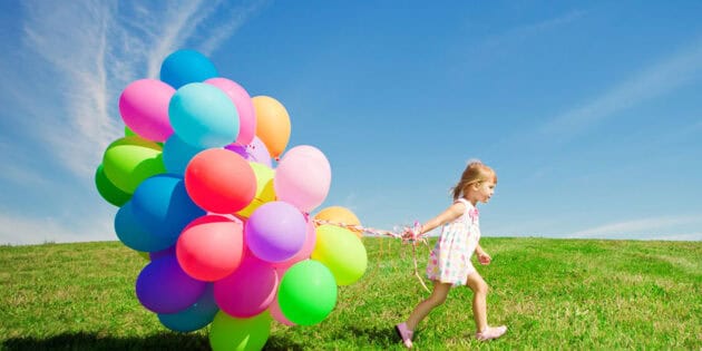 hapopy little girl holding colorful balloons on a green field